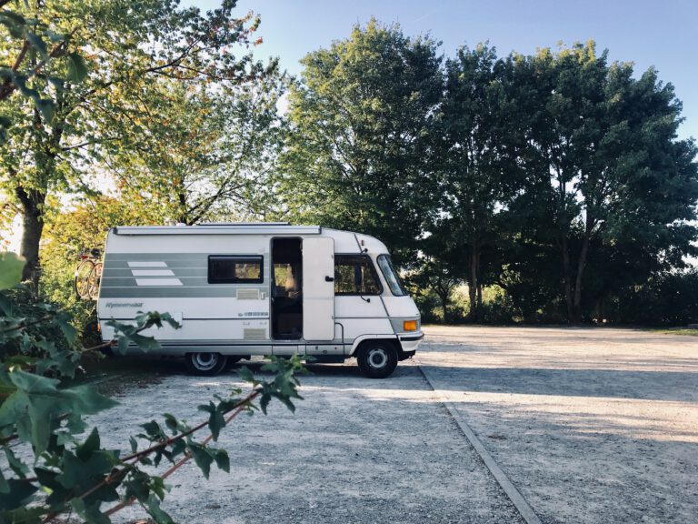 Camper op parkeerplaats naast groene bomen